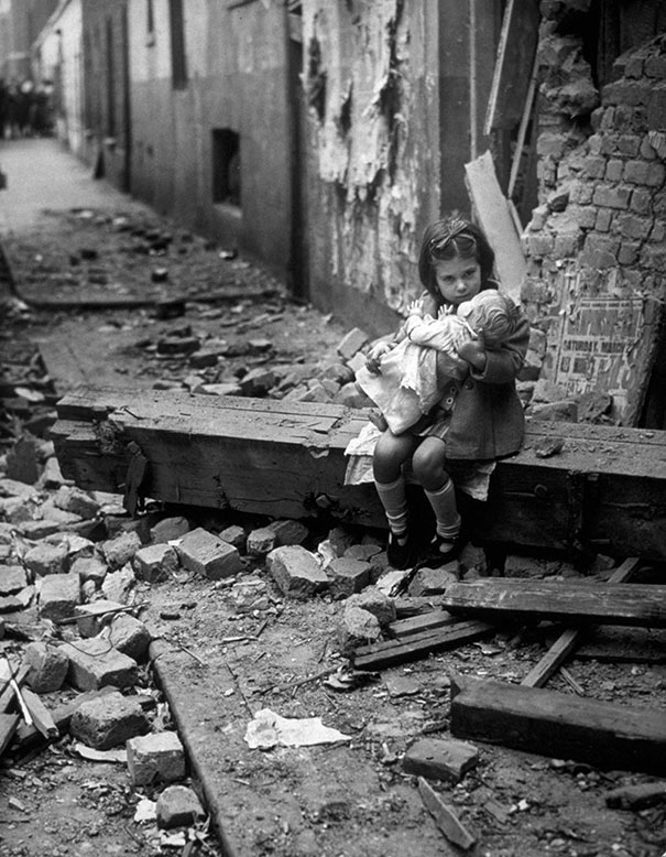 Little girl with her doll sitting in the ruins of her bombed home, London, 1940