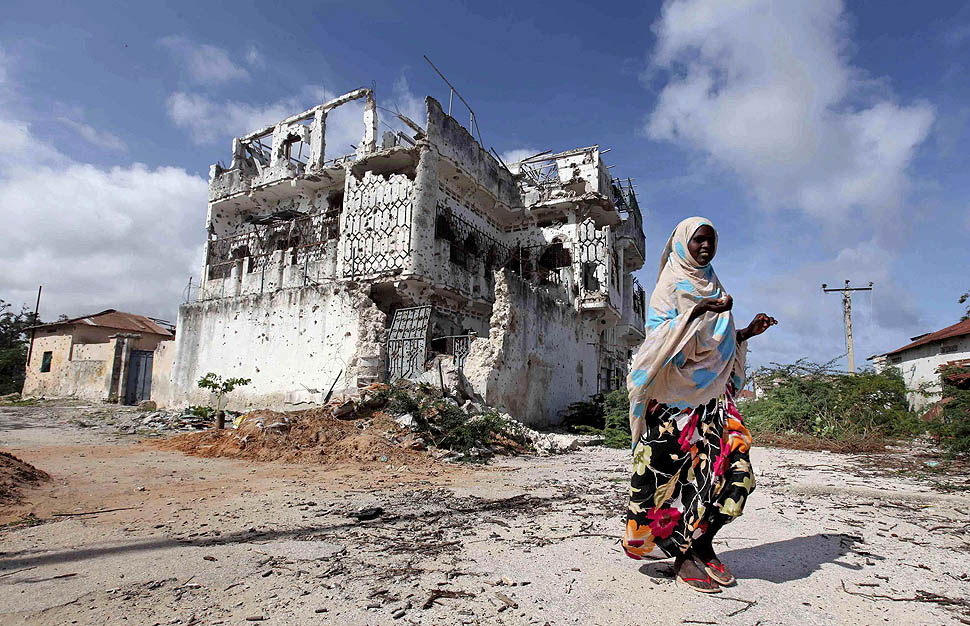 An internally displaced woman walks past a war-ravaged building in Howl Wadaag district of Mogadishu
